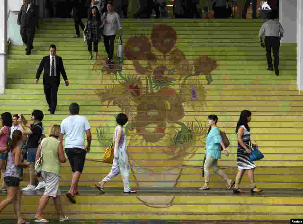 People walk on stairs featuring a five-meter-high reproduction of Vincent van Gogh's signature painting "Sunflowers",; at the entrance to Ocean Terminal in Hong Kong.