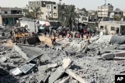 Warga Palestina berkumpul di dekat sebuah bangunan yang hancur akibat serangan udara Israel di kota Khan Younis, Jalur Gaza selatan, Jumat, 25 Oktober 2024. (AP)