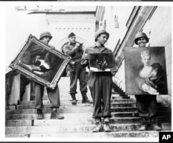 This photo provided by The Monuments Men Foundation for the Preservation of Art of Dallas, shows Monuments Man James Rorimer, with notepad, as he supervises American GI's hand-carrying paintings down the steps of the castle in Neuschwanstein, Germany in May, 1945.