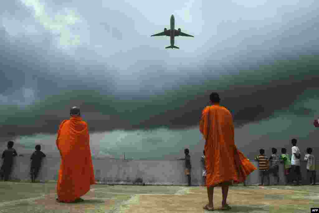 Buddhists monks and children look at an international passenger flight taking off at the Netaji Subhash Chandra Bose International Airport, from the rooftop at a Buddhist mission hostel and school for underprivileged children in in Kolkata, India.