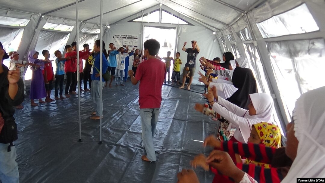 Para relawan dari Komunitas Pecinta Alam Malang Satu Jiwa, Jawa Timur, membawakan sesi pelajaran gempa bumi melalui permainan dan nyanyian di tenda kelas darurat SD Negeri Lolu, Kabupaten Sigi, Sulawesi Tengah, Kamis, 25 Oktober 2018. (Foto: VOA/ Yoanes Litha).