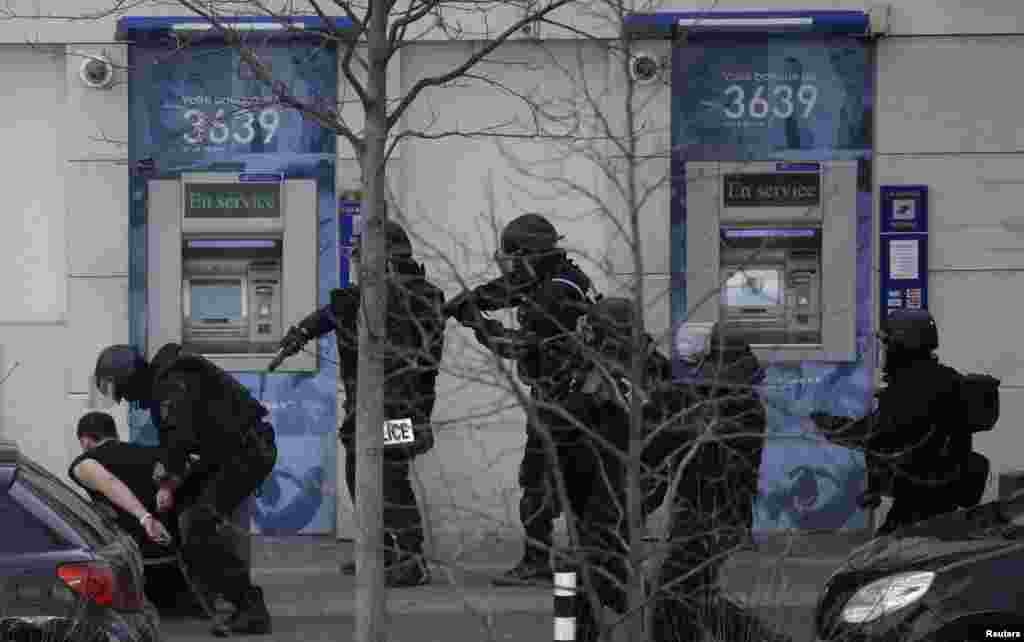 A suspect in a hostage taking situation is handcuffed by members of special French RAID forces outside the post offices in Colombes outside Paris, Jan. 16, 2015.