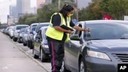 Volunteer Sharely Gomez marks the windshield after taking information from clients in their cars as they wait in line in before the food distribution begins at the West Houston Assistance Ministries Wednesday, Oct. 14, 2020, in Houston. (AP Photo/Michael