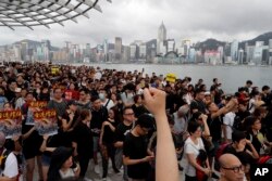 FILE - Protesters march near the skyline of Hong Kong, July 7, 2019. China’s central government has dismissed Hong Kong pro-democracy protesters as clowns and criminals while bemoaning growing violence surrounding the monthslong demonstrations.