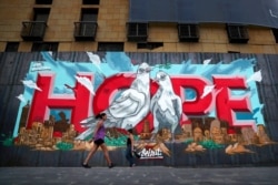 FILE - Women walk past graffiti painted on a metal barrier that closed the entrance of a hotel damaged by the Aug. 4 explosion in Beirut, Lebanon, Oct. 12, 2020.