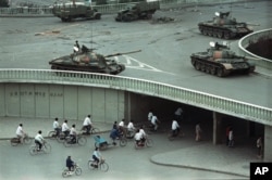FILE - Bicycle commuters, sparse in numbers, pass through a tunnel as above on the overpass military tanks are positioned in Beijing, China, two days after the Tiananmen Square massacre, on Tuesday morning, June 6, 1989.