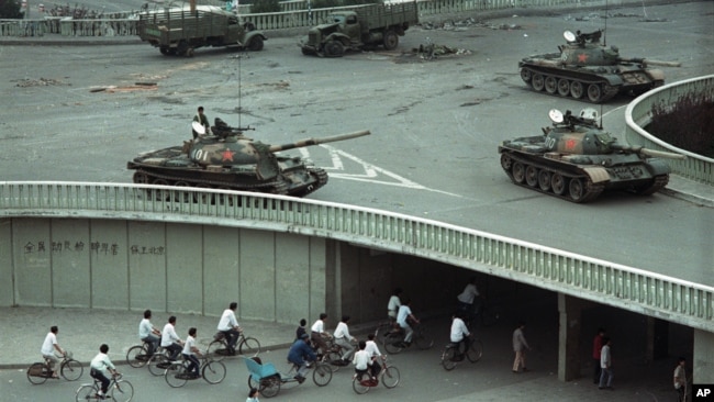 1989年6月6日星期二上午，在中国北京，天安门广场大屠杀发生两天后，自行车乘客稀少地穿过一条隧道，上面是天桥上部署的军用坦克。（美联社资料照片）