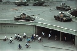 FILE - Bicycle commuters, sparse in numbers, pass through a tunnel as above on the overpass military tanks are positioned in Beijing, China, two days after the Tiananmen Square massacre, on June 6, 1989.