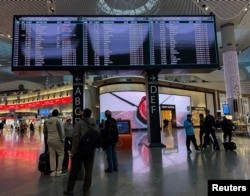 مسافران پس از فرود در فرودگاه بین‌المللی استانبول، به تابلوهای اطلاعات پرواز نگاه می‌کنند.