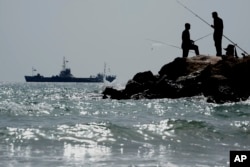 FILE—Men fish as in the background is seen a ship destined for Gaza rests in waters just outside the Cypriot port of Larnaca, Cyprus, on March 30, 2024