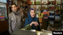 Nasser Abaidi (L), 34, an unemployed graduate, looks on while his mother speaks with journalists inside her shop in the impoverished Zhor neighborhood of Kasserine, where young people have been demonstrating for jobs.