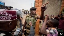 FILE - A policeman argues with a supporter of opposition leader Kizza Besigye at the gates of his party headquarters, before police who had surrounded it raided the building, in Kampala, Uganda, Feb. 19, 2016. 