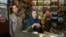 Nasser Abaidi (L), 34, an unemployed graduate, looks on while his mother speaks with journalists inside her shop in the impoverished Zhor neighborhood of Kasserine, where young people have been demonstrating for jobs.