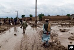 People walk near their damaged homes after heavy flooding in Baghlan province in northern Afghanistan on May 11, 2024.