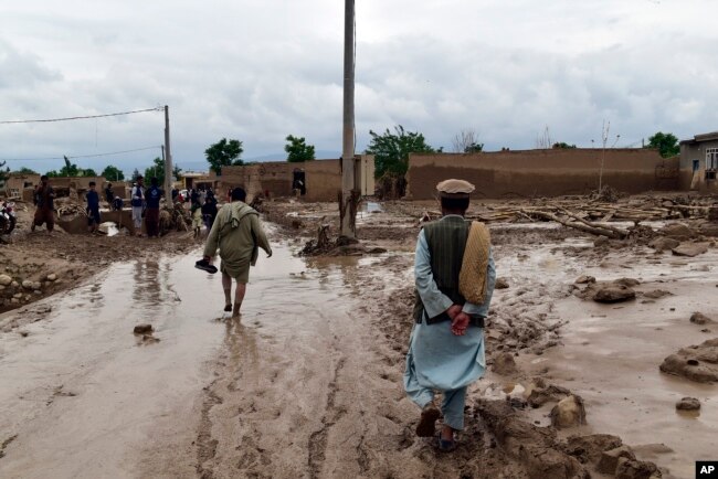 People walk near their damaged homes after heavy flooding in Baghlan province in northern Afghanistan on May 11, 2024.