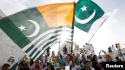 Para hadirin mengibarkan bendera nasional Pakistan dan bendera Kashmir, untuk mengekspresikan solidaritas dengan rakyat Kashmir, selama upacara perayaaan Hari Kemerdekaan ke-72 Pakistan di Mausoleum Muhammad Ali Jinnah di Karachi, Pakistan, 14 Agustus 2019.