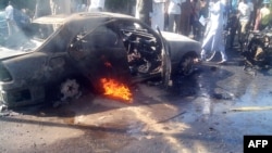 Residents stand on January 14, 2014 near a burning car in Maiduguri moments after at least 17 people were killed when an explosion ripped through a busy market in the mostly Muslim city in northeast Nigeria.
