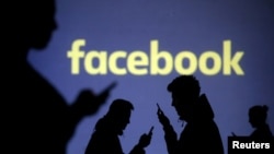FILE - Silhouettes of mobile users are seen next to a screen projection of Facebook logo in this picture illustration taken March 28, 2018.