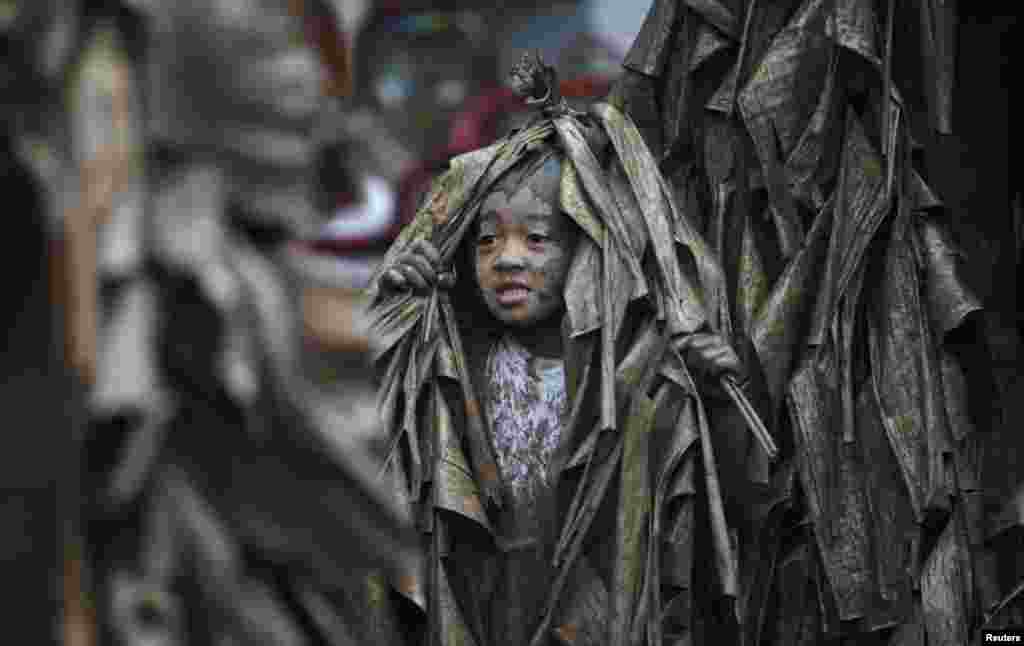 Seorang anak, ditutupi lumpur dan daun pisang kering, berjalan di sebuah desa untuk meminta lilin sebelum menghadiri misa merayakan hari raya Santo Yohanes sang Pembaptis di desa Bibiclat, Nueva Ecija, utara Manila, Filipina.