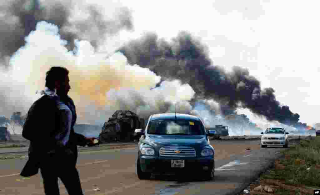 A rebel looks at burning vehicles belonging to forces loyal to Gadhafi, after an air strike by coalition forces, March 20, 2011. (Reuters)