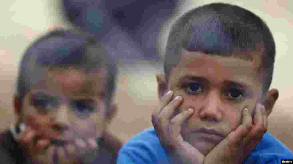 Kurdish refugee children from the Syrian town of Kobani sit behind a fence in a camp in the southeastern town of Suruc on the Turkish-Syrian border, Oct. 19, 2014. 