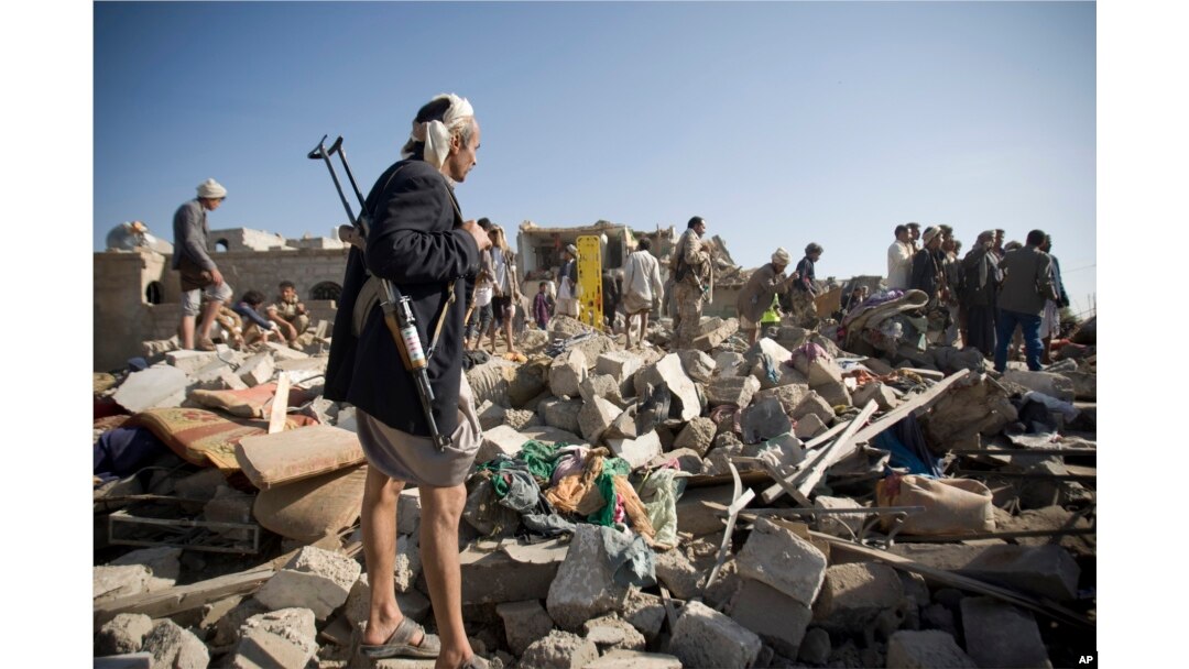 A Houthi Shi'ite fighter stands guard as people search for survivors amid the rubble of houses destroyed by Saudi airstrikes near Sana'a Airport, Yemen, March 26, 2015.