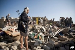 FILE - A Houthi Shiite fighter stands guard as people search for survivors under the rubble of houses destroyed by Saudi airstrikes near Sanaa Airport, Yemen, March 26, 2015