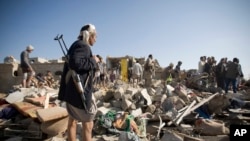 A Houthi Shiite fighter stands guard as people search for survivors under the rubble of houses destroyed by Saudi airstrikes near Sanaa Airport, Yemen, Thursday, March 26, 2015