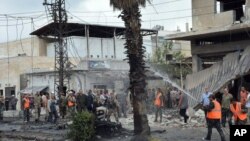 Pasukan Keamanan Suriah dan petugas pemadam kebakaran berkumpul di lokasi ledakan di pusat kota Homs, Suriah, 23 Mei 2017 (Sana via AP). 