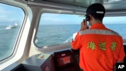 FILE - A Taiwanese coast guard member calls out on the megaphone for a Chinese coast guard ship at left to leave from the area around Kinmen County, Taiwan, July 11, 2024. Three crew members from a Chinese fishing boat were missing in the same area on Aug. 17, 2024.