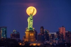 FILE - In this March 9, 2020, file photo, the full moon rises behind the Statue of Liberty in New York. From California to Colorado to Georgia and New York, Americans are taking a moment each night at 8 to howl to thank the nation's health workers.