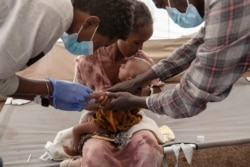 FILE - A Tigray woman who fled the conflict in Ethiopia's Tigray region, holds her malnourished baby as nurses give him IV fluids, at the Medecins Sans Frontieres (MSF) clinic, at Umm Rakouba refugee camp in Qadarif, eastern Sudan, Dec. 5, 2020.