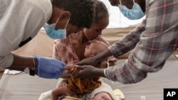 A woman who fled the conflict in Ethiopia's Tigray region holds her malnourished and severely dehydrated baby as nurses give him IV fluids, at the Medecins Sans Frontieres (MSF) clinic, at a refugee camp in Sudan, Dec. 5, 2020.