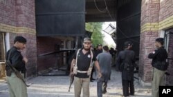 Policemen gather near a damaged jail gate after inmates escaped from the prison in the city of Bannu, Pakistan's northwest, April 15, 2012. 