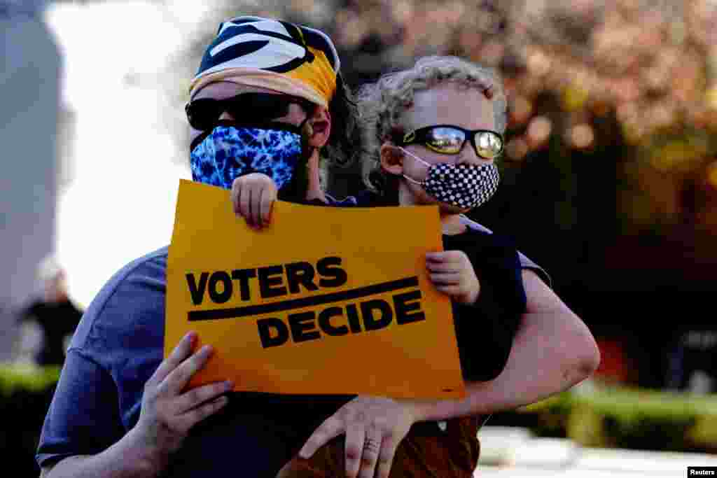 A Biden supporter holds a sign reading &quot;voters decide&quot; at a &#39;Stop the Steal&#39; protest held by supporters of U.S. President Donald Trump in Madison, Wisconsin, Nov. 7, 2020. 