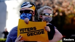 A Biden supporter holds a sign reading 'Voters decide' at a protest held by supporters of US President Donald Trump outside the Wisconsin State Capitol on Nov. 7, 2020.