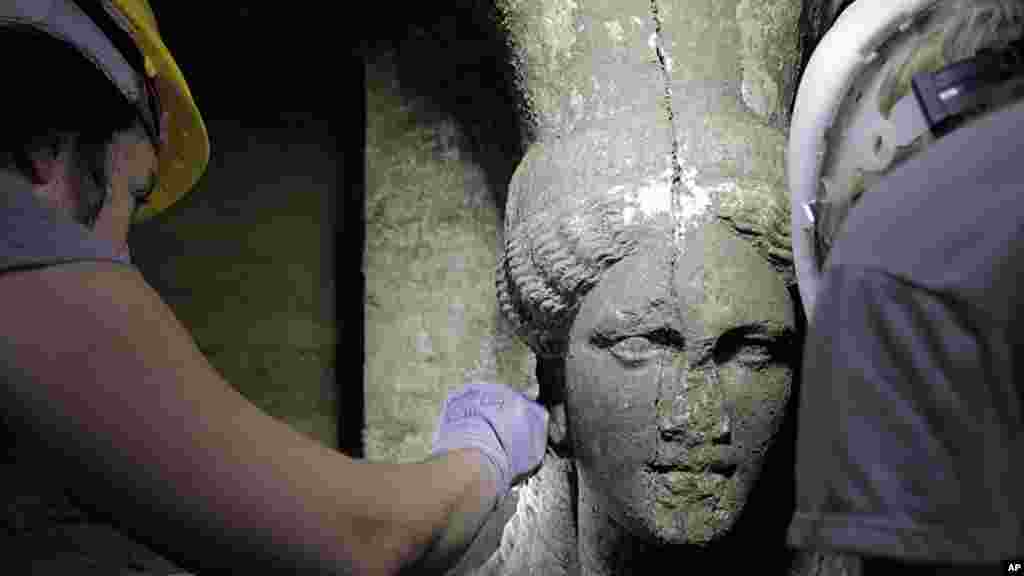 Archaeologists inspect a female figurine in a hall leading to an unexplored main room of an ancient tomb, in the town of Amphipolis, northern Greece, released by the Greek Culture Ministry, Sept. 7, 2014.