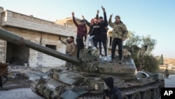 Pendukung oposisi Suriah berdiri di atas tank tentara Suriah yang direbut di Kota Maarat al-Numan, barat daya Aleppo, Suriah, 30 November 2024. (Foto: AP)