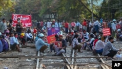 In this Feb. 17, 2021, file photo, demonstrators with placards sit on the railway tracks in an attempt to disrupt train service during a protest against the military coup in Mandalay, Myanmar. (AP Photo/File)
