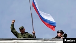 Un hombre ondea una bandera rusa en el techo de una base naval en Sebastopol, la cual fue tomada por fuerzas pro-rusas.