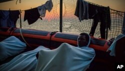 FILE - migrants rest on the deck of the Open Arms boat, after being rescued off the coast of Libya in the early hours of the night of Thursday, Aug. 2, 2018.