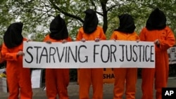 Protesters depicting detainees of the US detention facility at Guantanamo Bay, Cuba, hold a banner, during a demonstration outside the US embassy in central London, May 18, 2013.