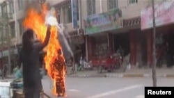 A woman throws a white scarf over Tibetan Buddhist nun Palden Choetso as she burns on the street in Daofu, China - or Tawu in Tibetan - November 3, 2011.