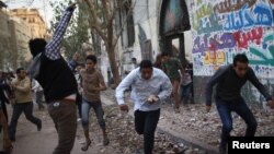 A protester throws stones as others run for cover during clashes with riot police at Tahrir Square in Cairo, November 26, 2012.