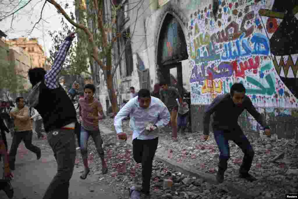 A protester throws stones as others run for cover during clashes with riot police at Tahrir Square in Cairo, November 26, 2012. 