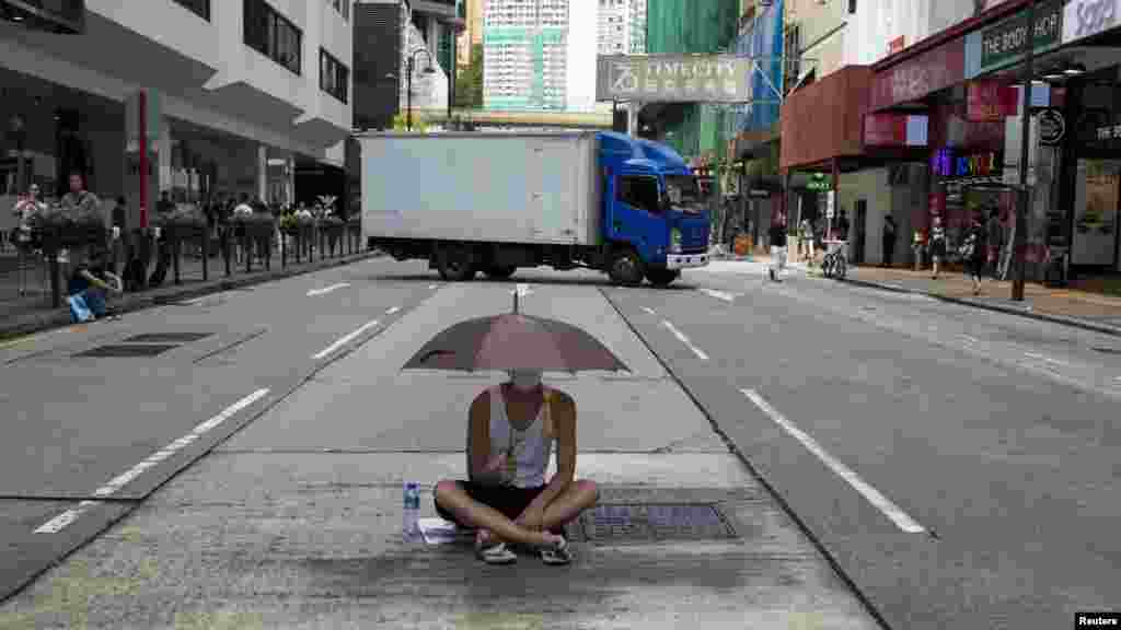 A protester sits under an umbrella as he attends a rally along a main street at Hong Kong's shopping district Tsim Sha Tsui, Oct. 1, 2014. 