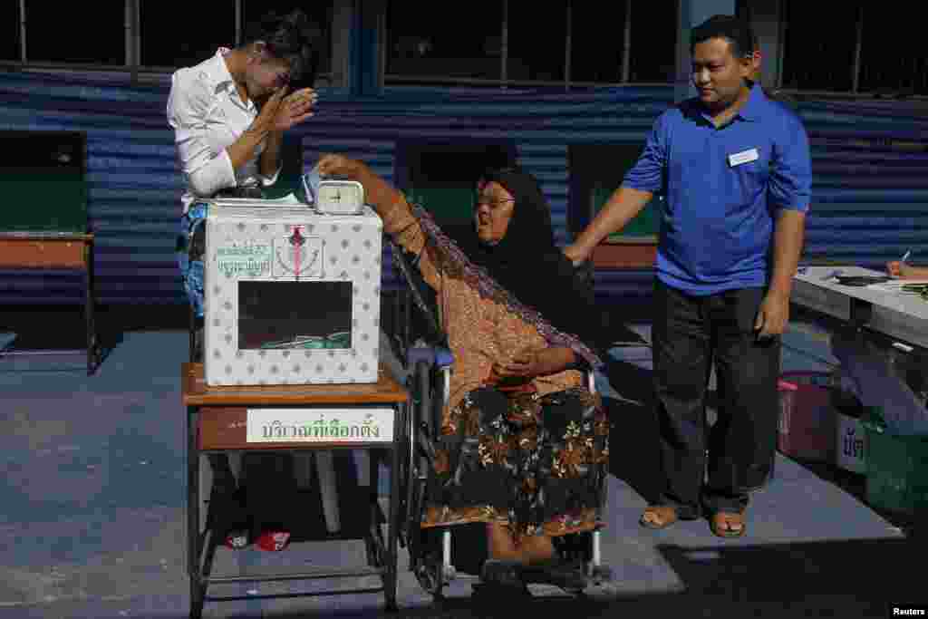 An election official greets a woman in a wheelchair as she casts her ballot at a polling station in Bangkok, March 30, 2014.