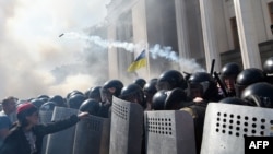 FILE - A demonstrator holds a police officer's shield in front of the parliament building in Kyiv as smoke rises from the building during clashes with police officers on August 31, 2015.