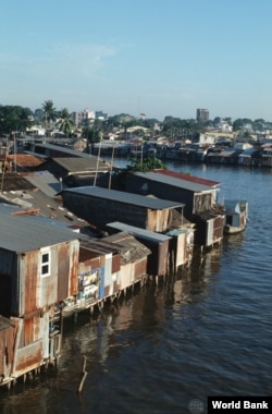 Perumahan kumuh di Sungai Saigon, dengan latar belakang kota Saigon. Perencanaan tata kota bertujuan meminimalisir daerah kumuh yang disebabkan oleh migrasi dari pedesaan (Bank Dunia)