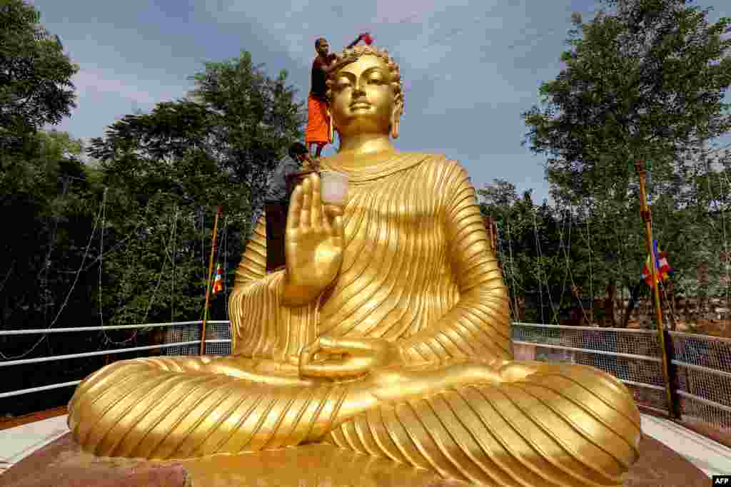 A Buddhist monk climbs atop a giant statue of Buddha to wash and decorate on the eve of Buddha Purnima, a holiday traditionally celebrated for Buddha&#39;s birthday also known as Vesak celebrations, in Bhopal, India.